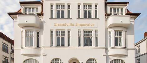A large, white building with the name "Strandvilla Imperator" on the facade. It has multiple windows, a central entrance with an arch, and balconies on the upper floors.