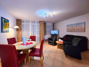 A living room with a dining area, a TV, and a painting on the wall. - 2 Room B 010 - Wohnpark Binz (with indoor pool) (Binz)