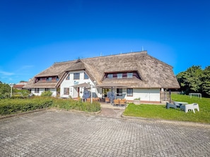 Een traditioneel gebouw met rieten dak, een overdekt terras en een geplaveid voetpad.