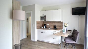 Eine moderne Küche mit weißen Schränken, einer Holz Arbeitsplatte und einer eingebauten Mikrowelle. Es gibt einen Essbereich mit Tisch und Stühlen sowie einen an der Wand montierten Fernseher.
