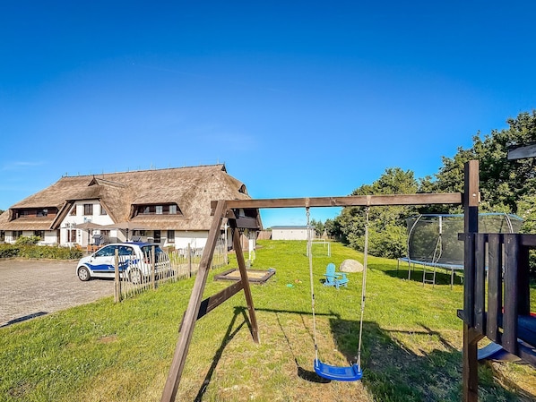 Een huis met rieten dak, een schommel en een auto op de oprit.