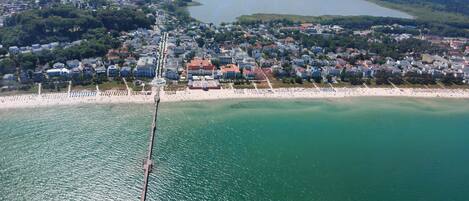 An aerial view of a coastal town with a pier extending into the water, surrounded by residential buildings and a beach.