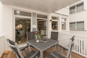 An outdoor patio with a table and chairs, a white railing, and a view into the house.