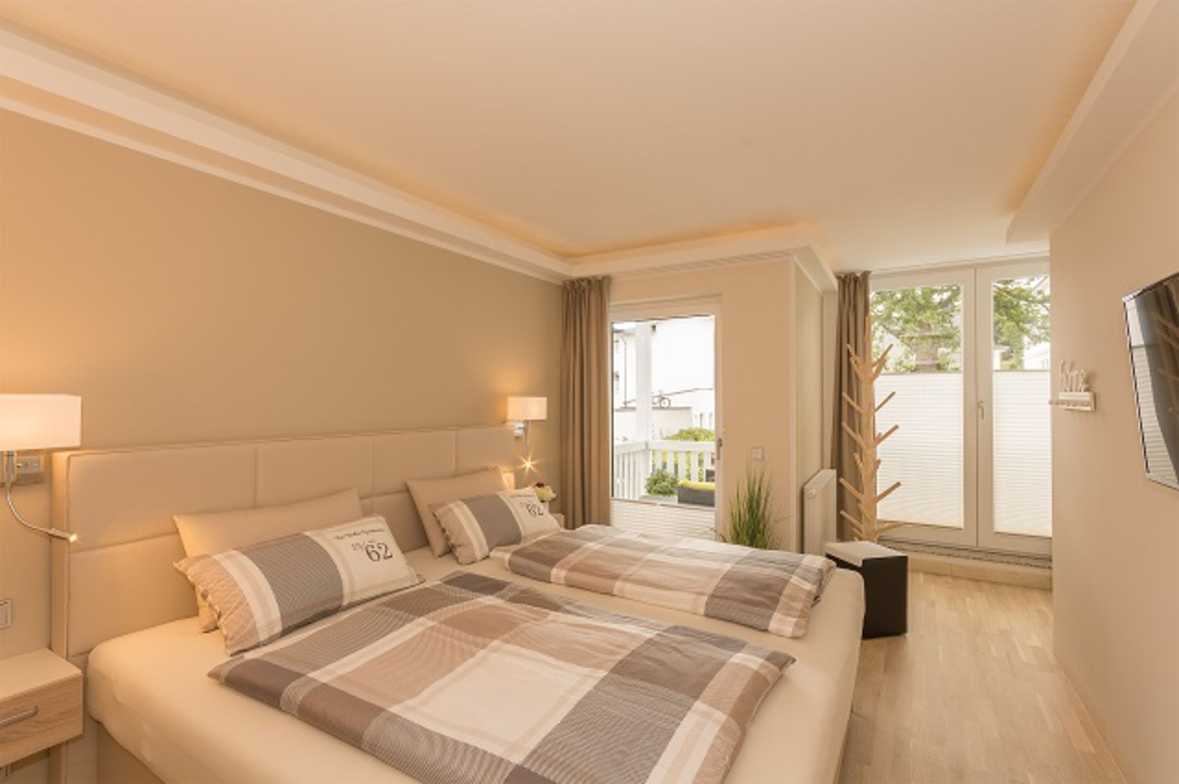 A hotel room with a large bed, two bedside lamps, a window with a view, and a small plant.