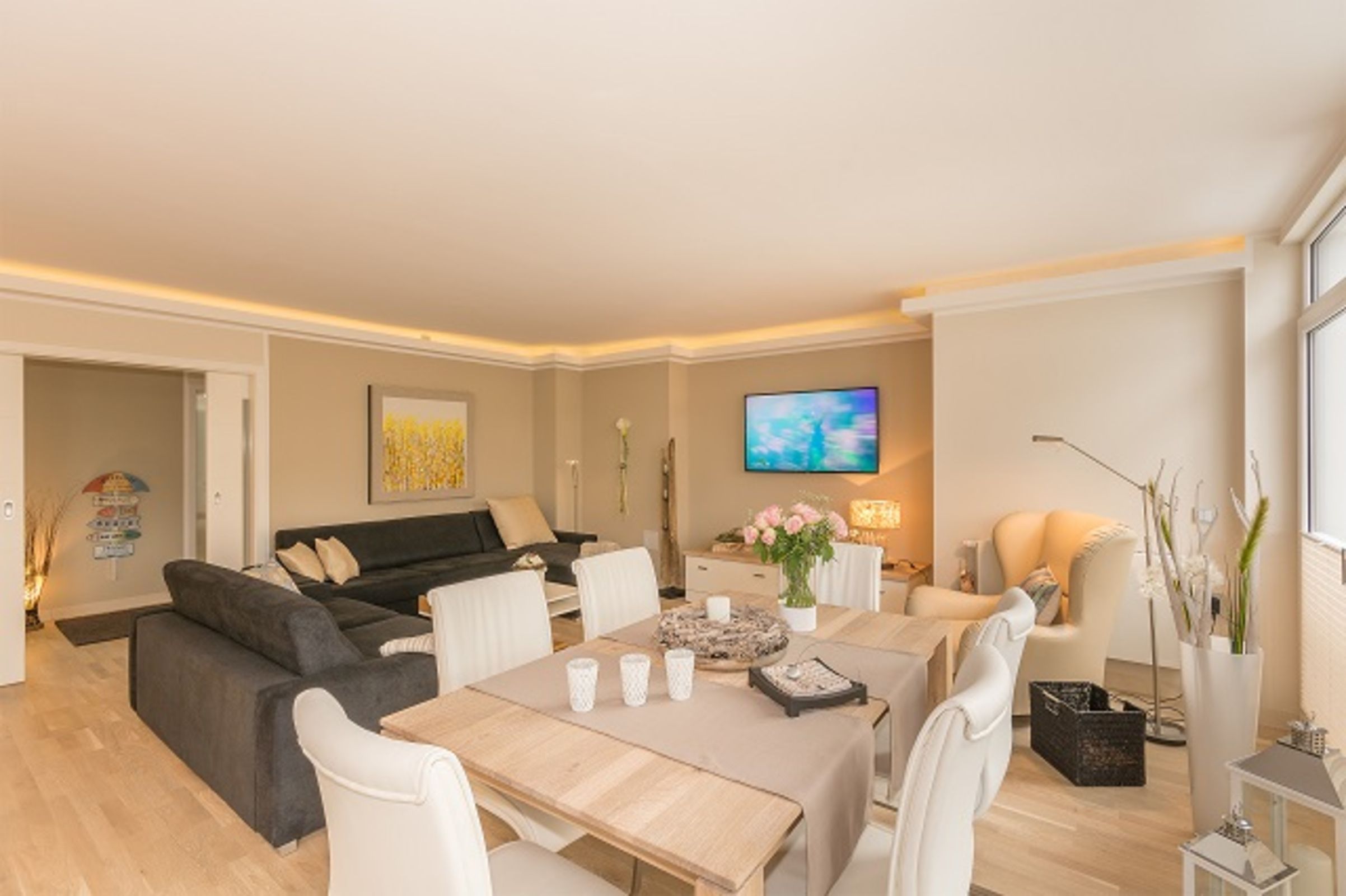 A modern living room with a dining area, a flat-screen TV, and a sofa.