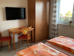 A bedroom with a bed, a desk with a chair, a television, and a wardrobe.