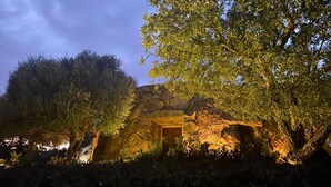 A stone building with a doorway, surrounded by trees and illuminated by warm lighting. - Il Nuraghe Del Lago Coghinas (Oschiri)