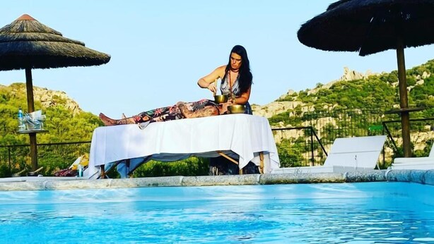 A person relaxing by a poolside table with a drink, surrounded by umbrellas and a scenic view. - Il Nuraghe Del Lago Coghinas (Oschiri)