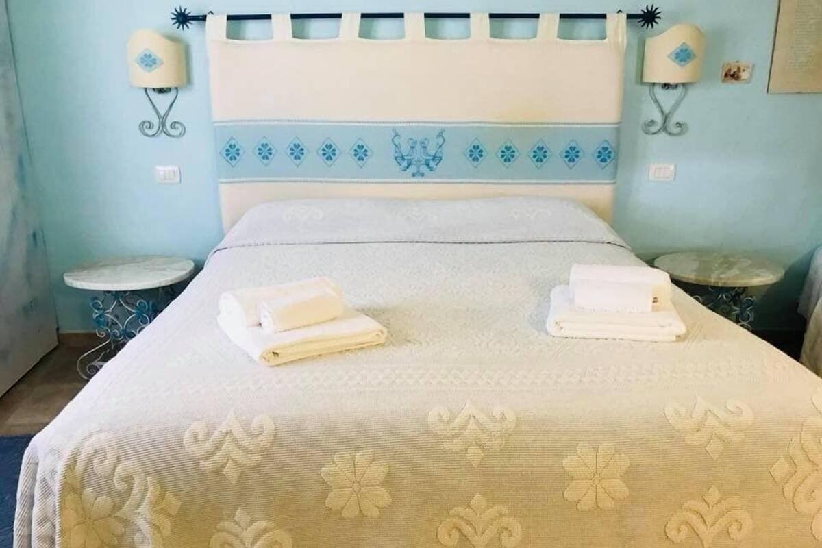 Un lit bien fait, avec des serviettes pliées, une couvre-lit à motifs et deux lampes fixées au mur.