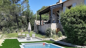 Piscina retangular com deck branco, rodeada por grama sintética verde.