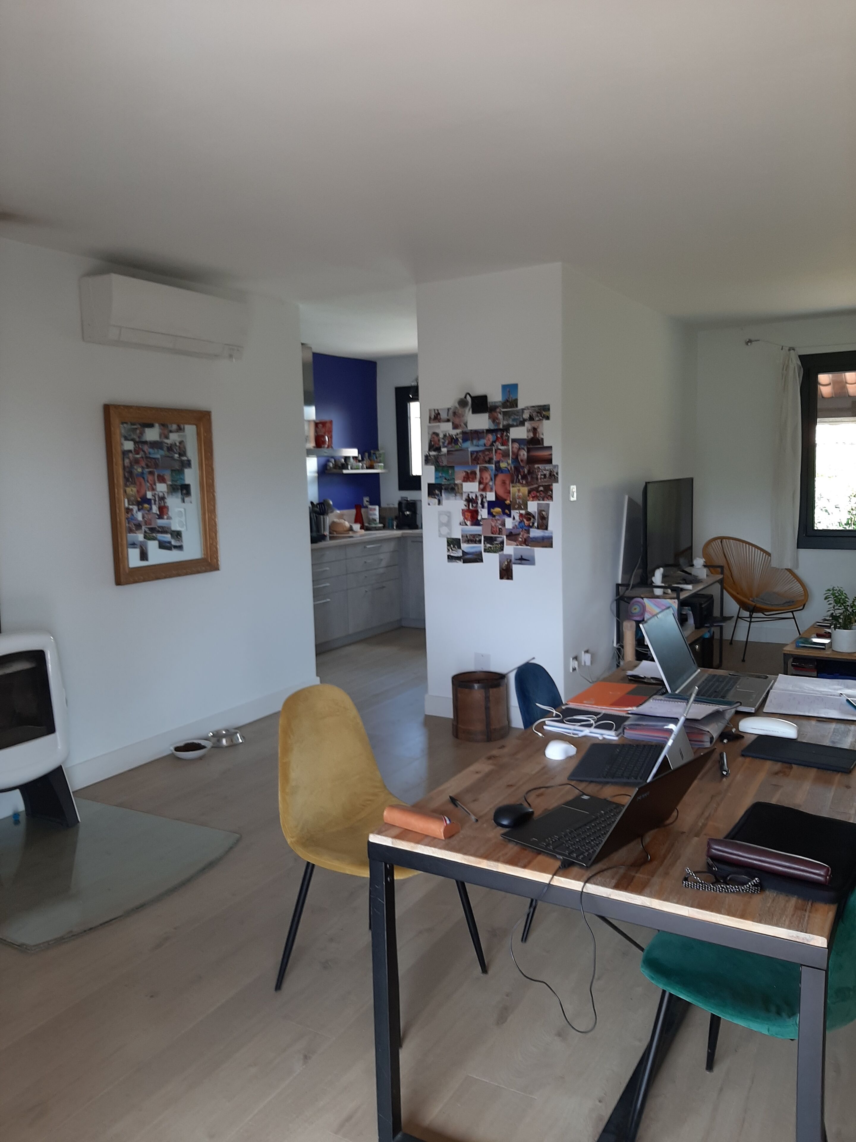 Ein zeitgemäßer Wohnraum mit einem Holzesstisch, einem gelben Sessel, einem Laptop auf dem Tisch und einer Wand mit Fotos.