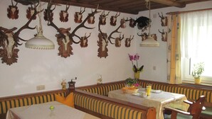 Un espace repas avec des bancs et des tables en bois, décoré de trophées de chasse aux murs et de lampes suspendues.