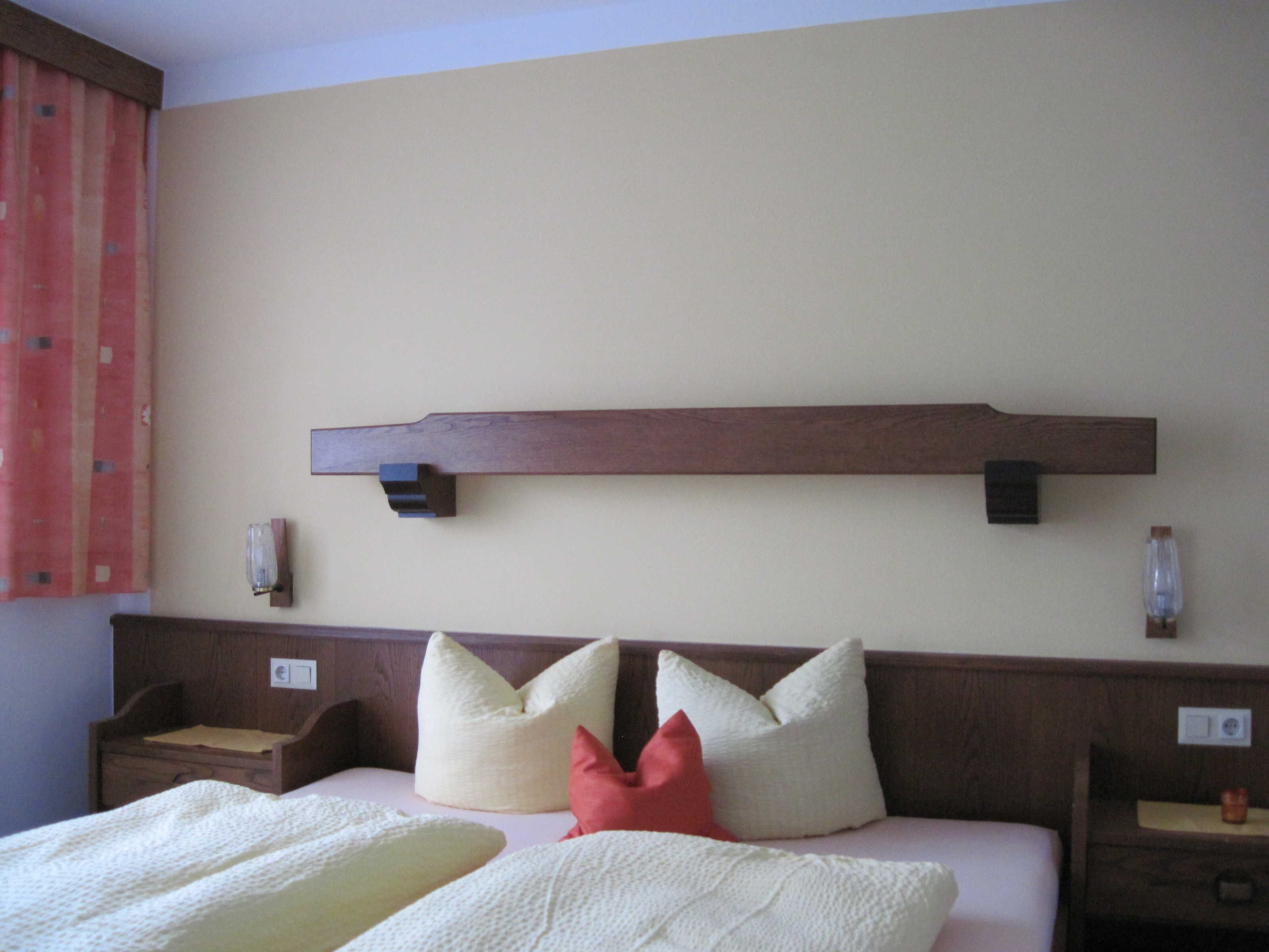 Une chambre d’hôtel avec un lit, des oreillers, une table de chevet et une étagère fixée au mur.
