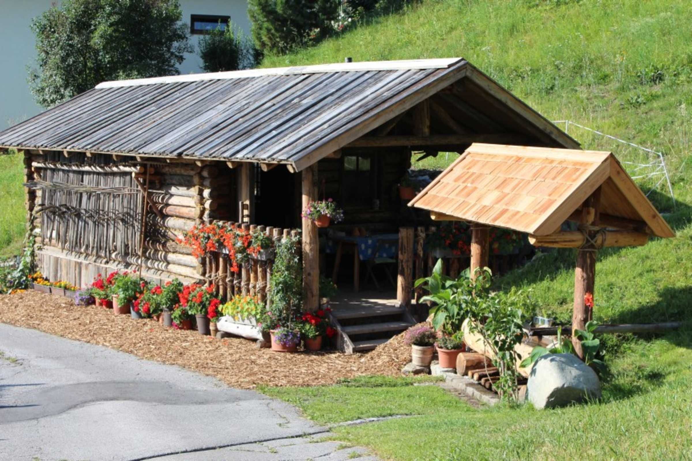Un chalet rustique en rondins de bois, doté d’un porche en bois, et entouré de plantes et de fleurs en pot.