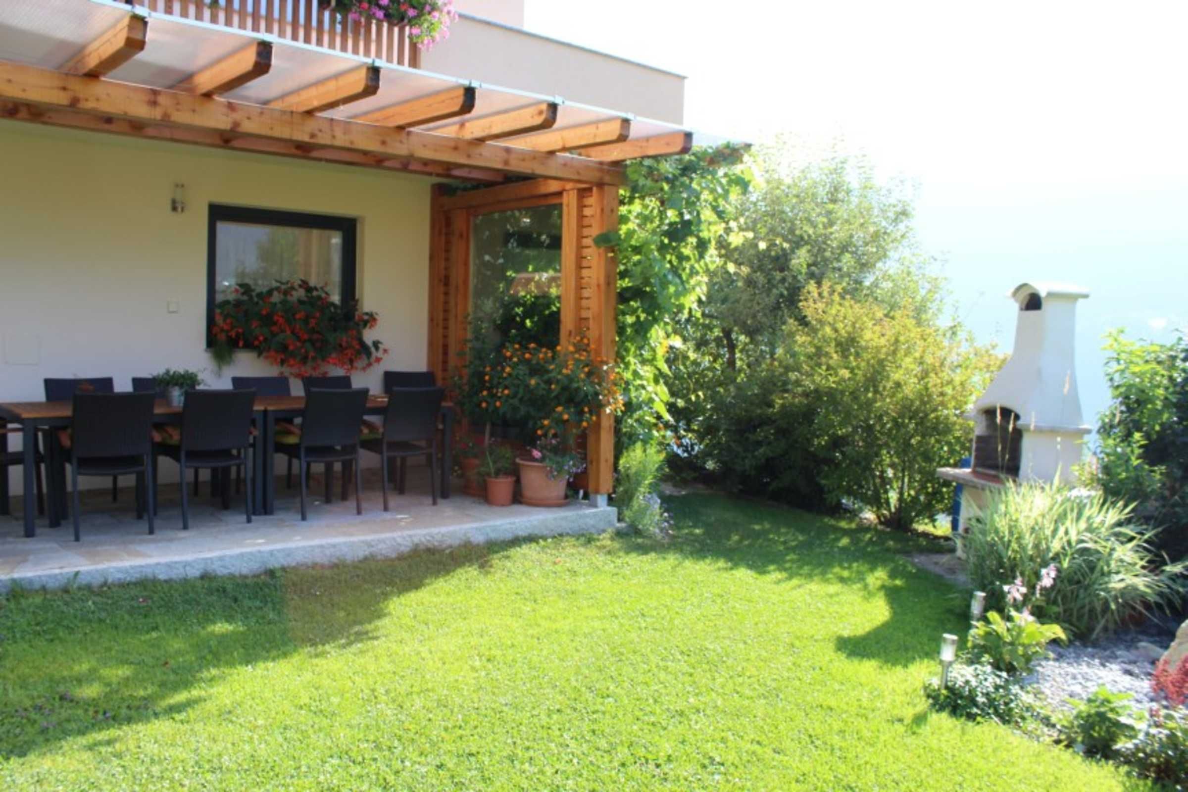 Une terrasse dotée d’une pergola en bois, d’une table à manger avec des chaises et de plantes en pot.
