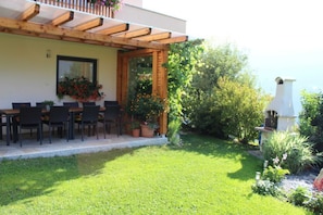 Une terrasse dotée d’une pergola en bois, d’une table à manger avec des chaises et de plantes en pot.