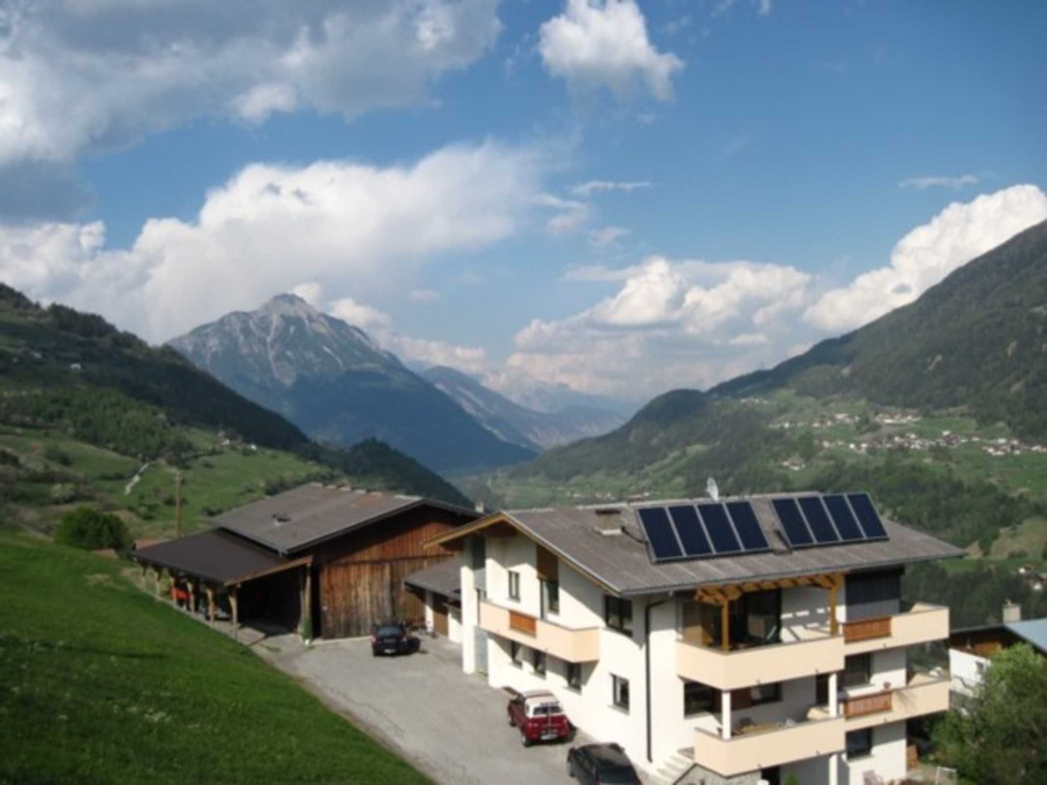 Un bâtiment moderne à deux étages, doté d’un garage, de panneaux solaires et offrant une vue sur les montagnes.