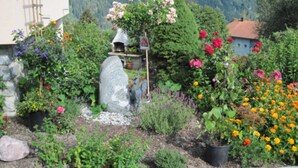 Un jardin avec différentes plantes et fleurs, une structure en pierre et un bâtiment avec un toit rouge.
