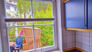 A kitchen with a large window, a dining area with outdoor furniture, and a view of greenery and buildings outside. - 3 room A + 0 - Wohnpark Binz (with indoor pool) (Binz)