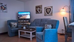 A living room with two blue armchairs, a coffee table, and a television on the wall. - 3 room A + 0 - Wohnpark Binz (with indoor pool) (Binz)