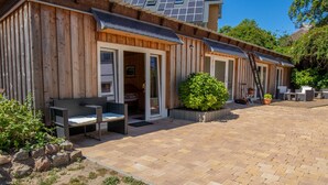 Ein Holzhaus mit Terrasse, Sitzgelegenheiten im Freien und einem kleinen Garten.