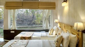 Une chambre avec une grande fenêtre, un lit recouvert de draps blancs, une tête de lit en bois et un climatiseur fixé au mur.