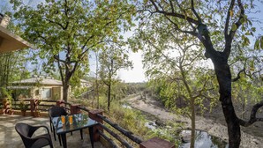 Une terrasse extérieure avec une table et des chaises, donnant sur une rivière et des arbres.
