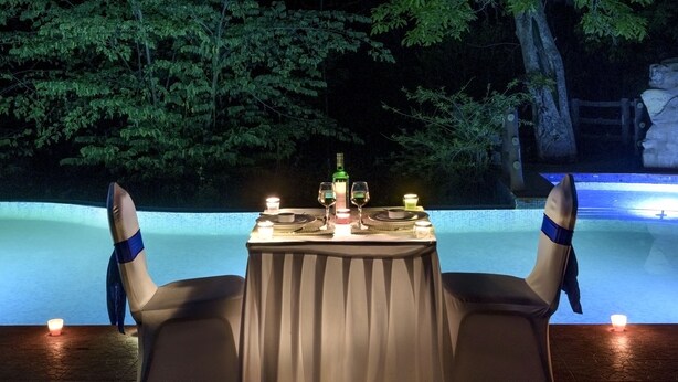 Un espace de restauration en plein air avec une table, des chaises et des bougies, entouré d’arbres et d’une piscine.