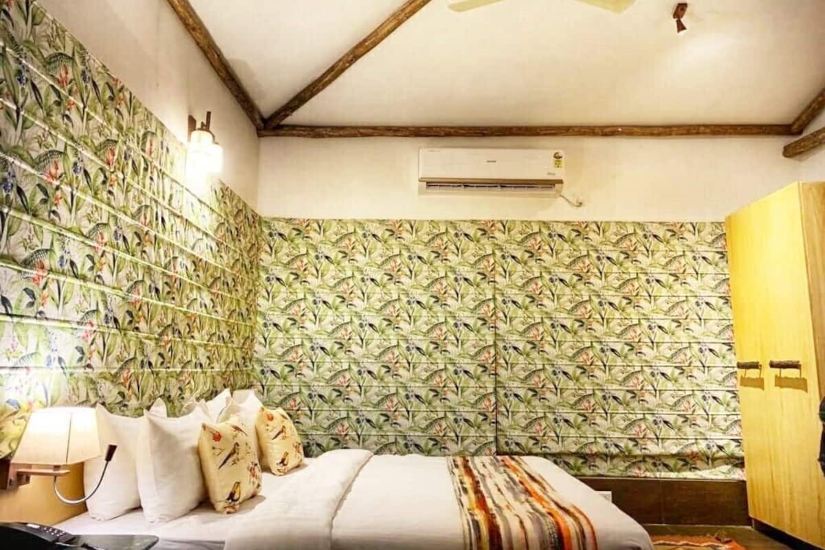 Une chambre avec un lit, un ventilateur de plafond, un appareil de climatisation et un mur orné d’un motif végétal.