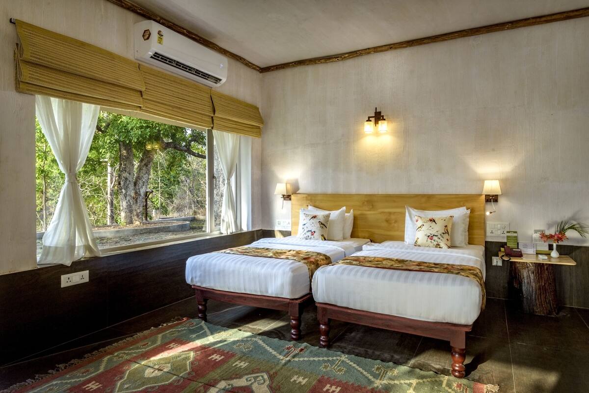 Une chambre avec deux lits, une grande fenêtre avec des rideaux, un appareil de climatisation et une table de chevet avec une lampe.