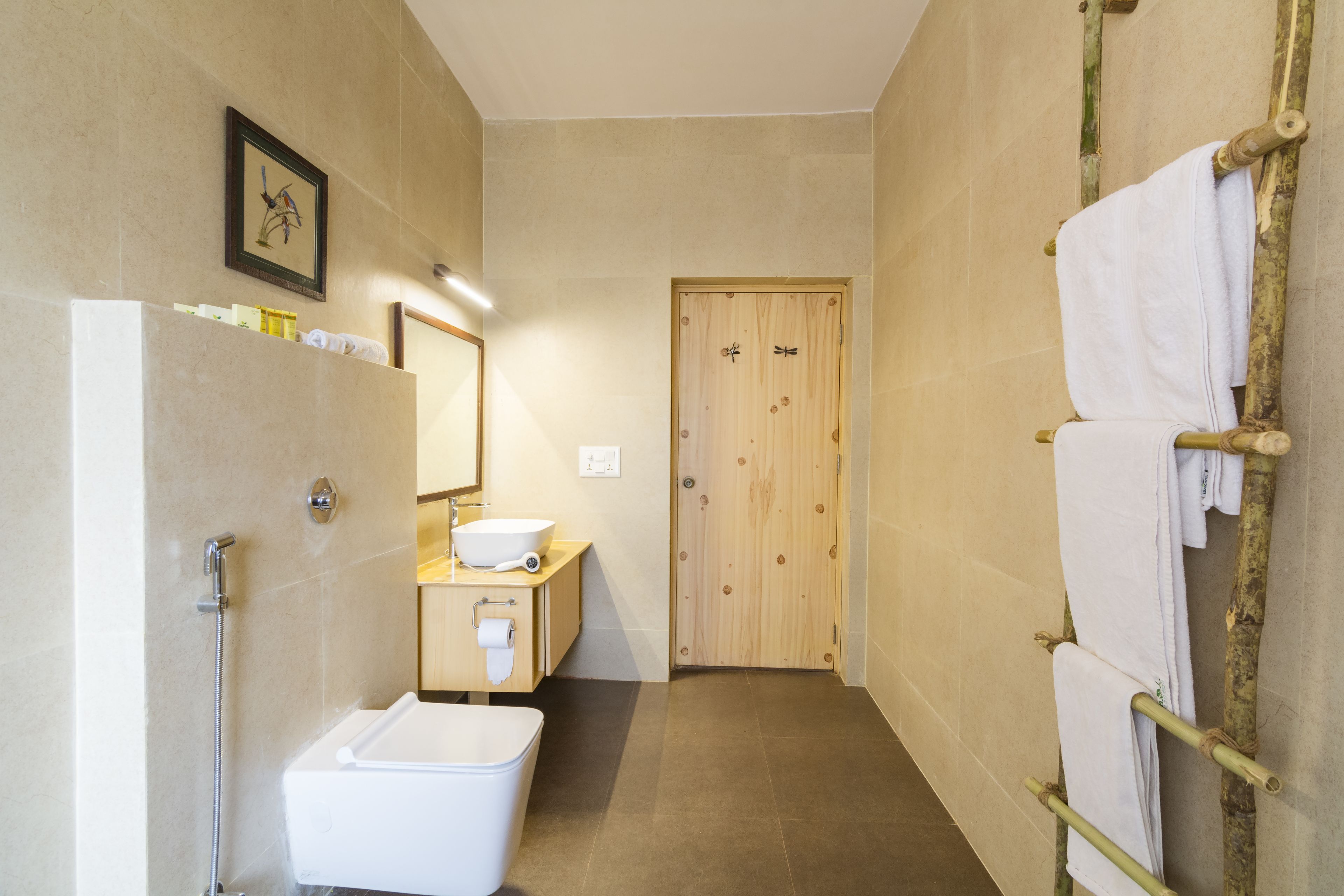 Baño pequeño con ducha, lavamanos e inodoro. Se aprecia una puerta de madera y un perchero a la derecha.