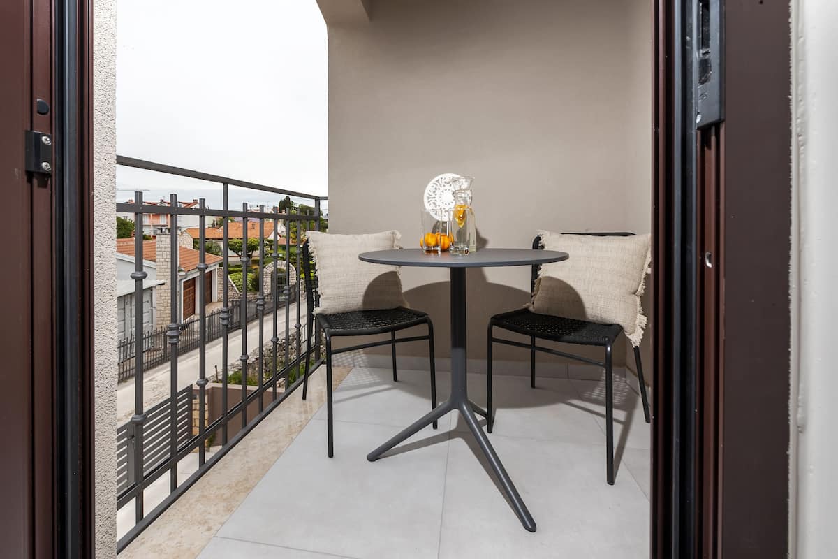 A balcony with a round table and two chairs, a decorative glass pitcher, and a white doily.