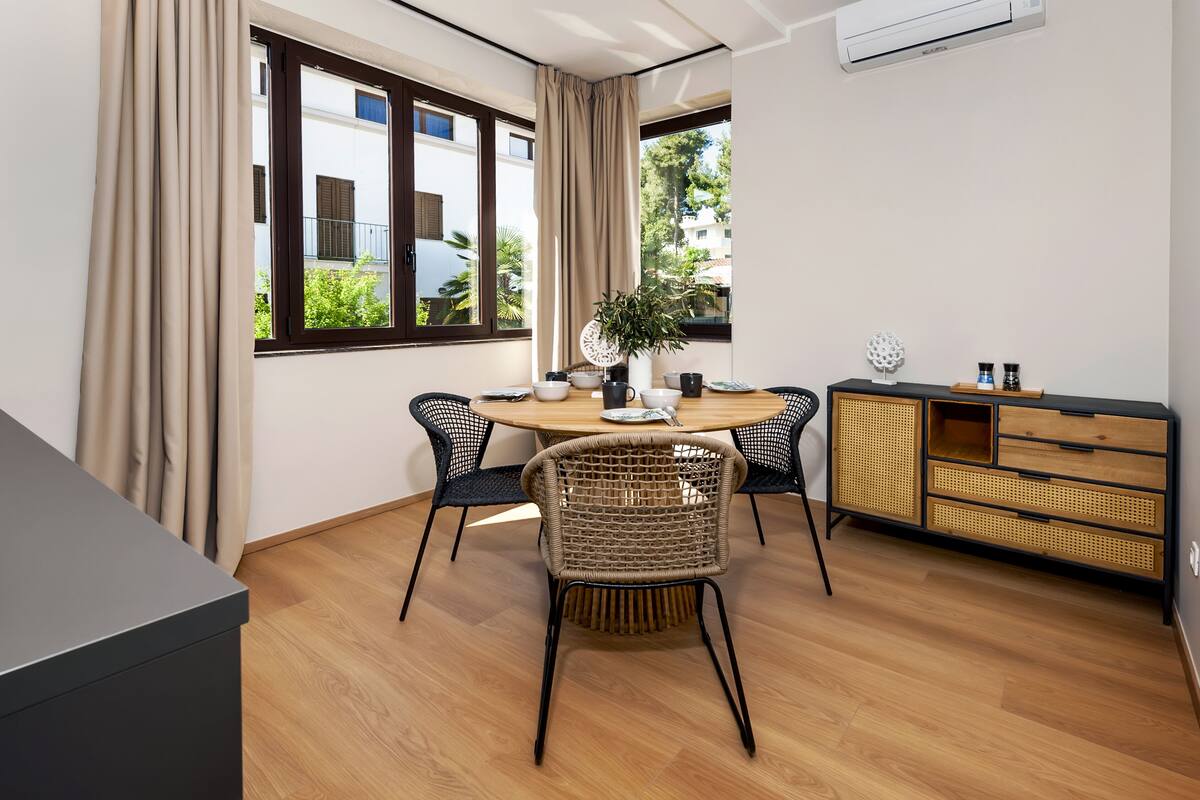 A modern dining area with a round table, four chairs, a buffet cabinet, and a potted plant.