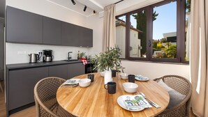 A modern kitchen with dark cabinets, a round wooden table, wicker chairs, and a large window with curtains. - Villa Tomo (Rovinj)