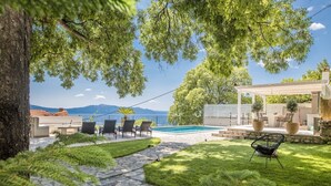 A backyard with a stone pathway, a pool, outdoor furniture, and a pergola with seating. - Villa Ana – Private Villa mit beheiztem Pool, großem Garten & Meerblick… (Zaostrog)