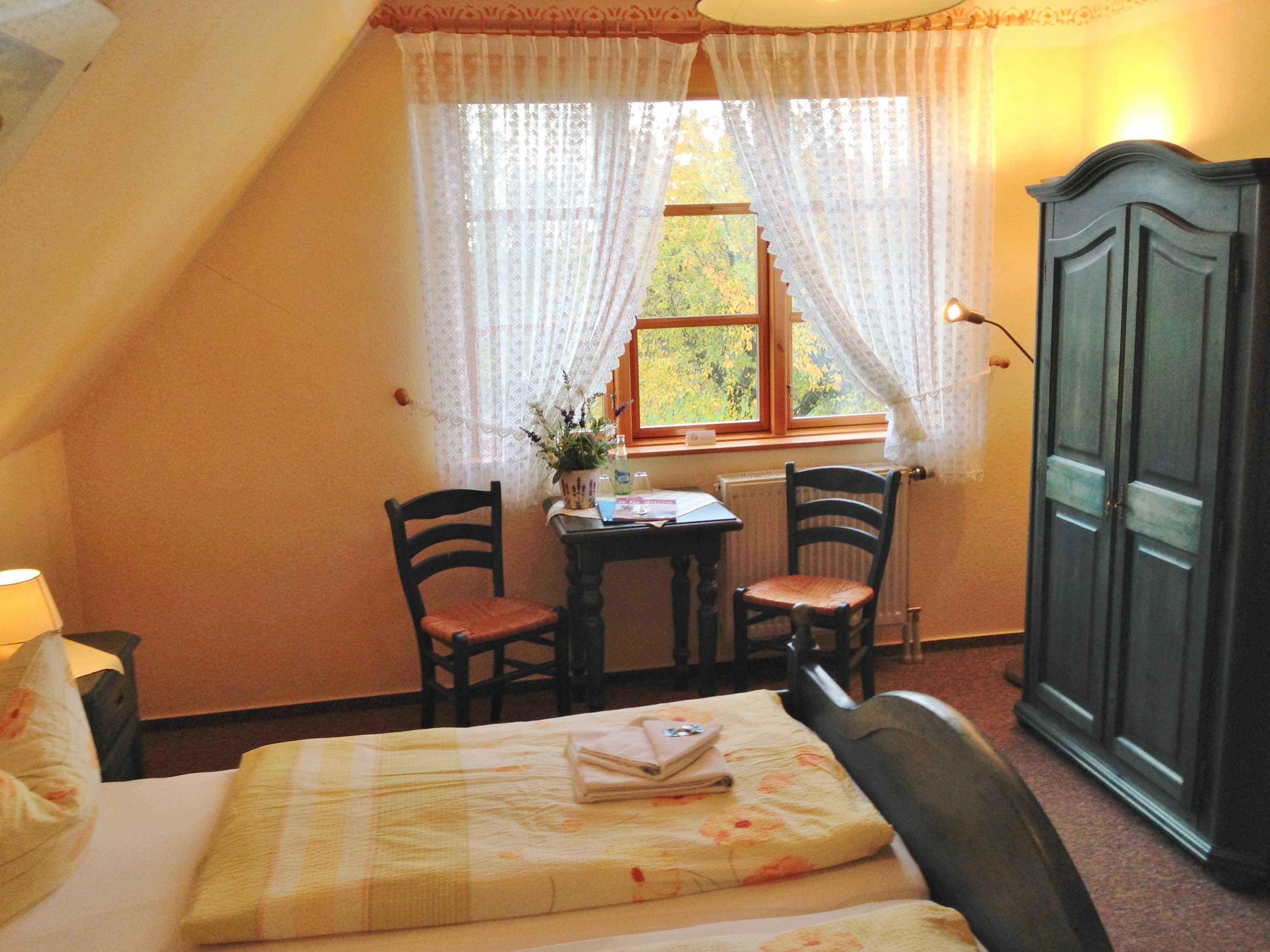 A small, cozy room with a bed, two chairs, a table, and a cabinet.
