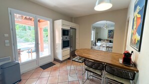 A kitchen with a wooden table, two bar stools, a refrigerator, and an oven. - Villa Terre de Provence - Pool & Garden Clim prox Golf- Saint-Raphaël (Saint-Raphaël)