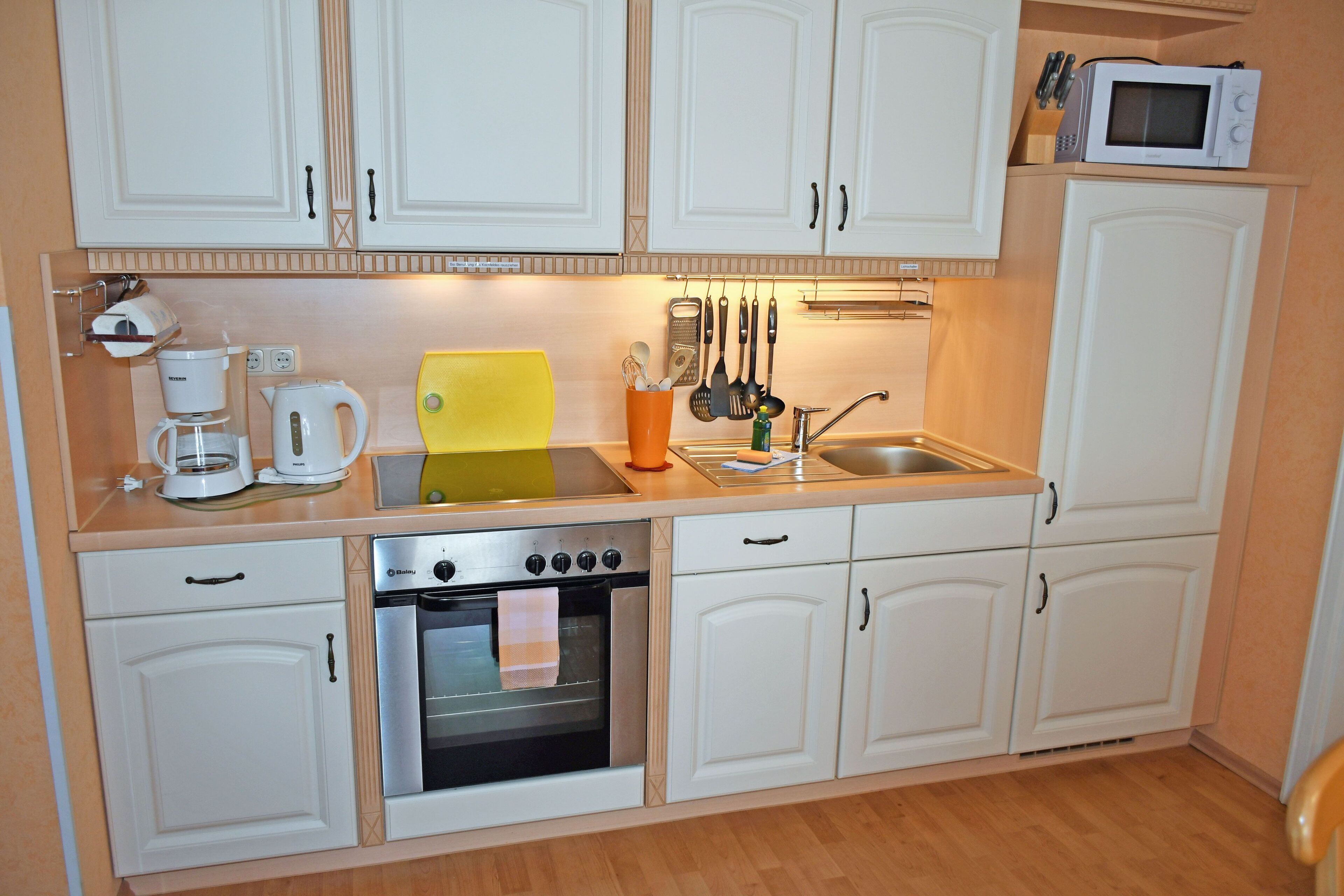 A compact kitchen with white cabinets, a coffee maker, a microwave, and various utensils.