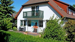 A two-story house with a balcony, a small garden, and a mural of a sailboat on the front wall.