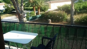Un balcón con una mesa y sillas blancas, con vistas a un jardín con árboles y un edificio blanco.