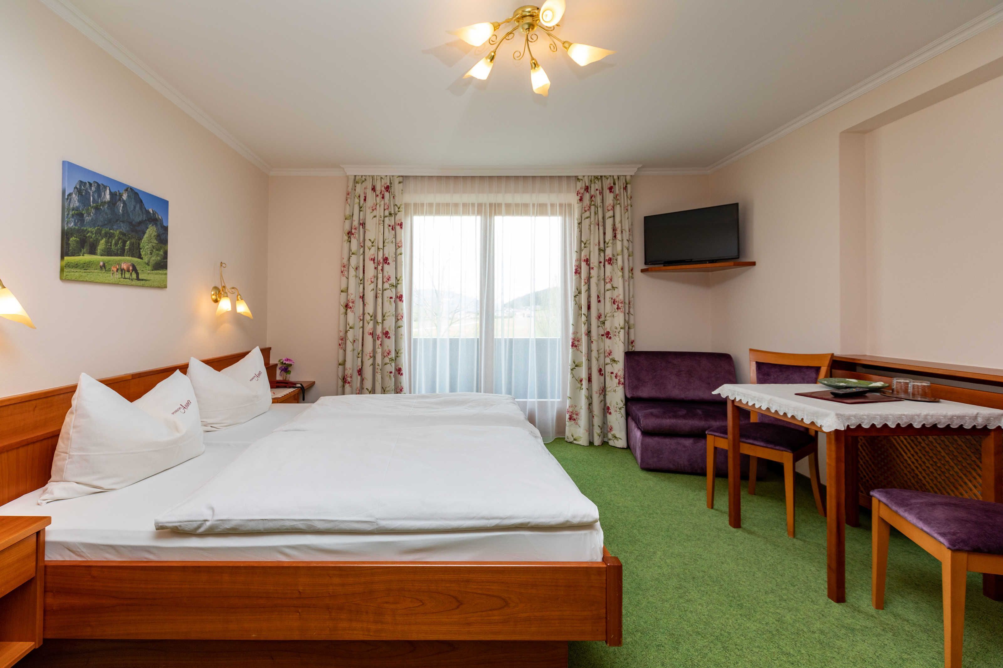 A hotel room with a bed, a desk with a chair, a television, and a window with curtains.