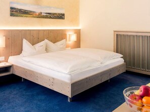 Una habitación de hotel con una cama de madera, dos lámparas de noche, un radiador y un frutero al lado.