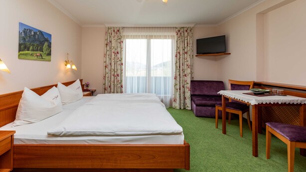Habitación de hotel con cama, escritorio con silla, televisión y ventana con cortinas.