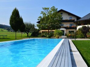 Una piscina con muelle de madera, una casa con balcón y un césped.
