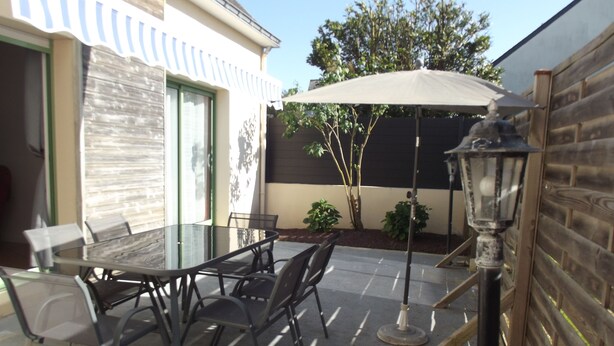 An outdoor patio with a glass table and chairs, a wooden fence, and a lamp post. - House in the heart of the marshes (Saillé Guérande)