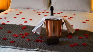 A bed with rose petals scattered on a textured bedspread, a copper bucket, and a white cloth draped over it.