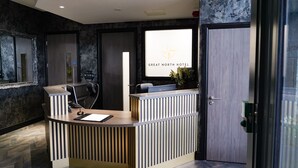 Een modern ontworpen receptiebalie, een groot raam met de hotelnaam, en een deur aan de rechterkant.