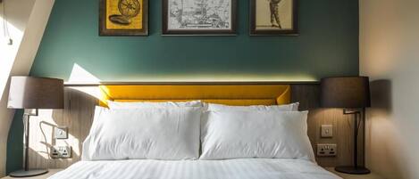 A hotel room with a bed, two bedside lamps, a wall-mounted map, and a framed picture.