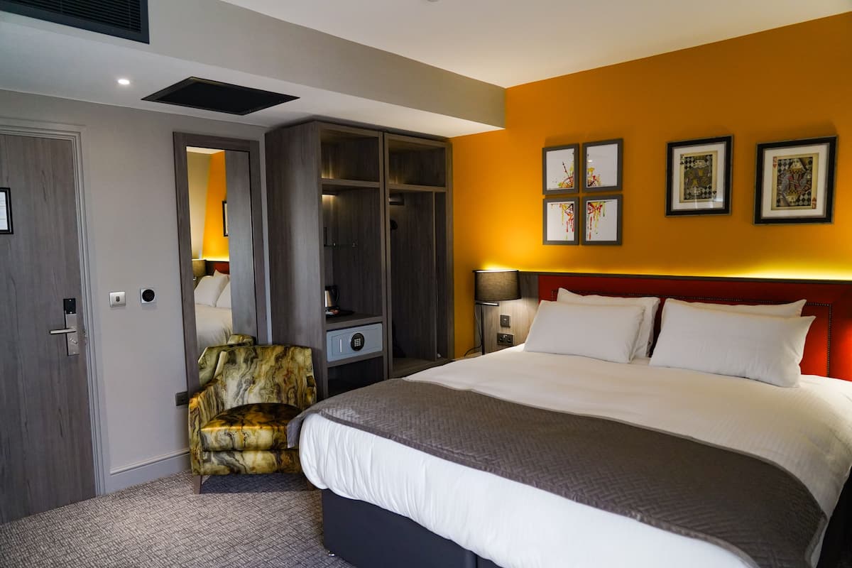 A hotel room with a large bed, a wardrobe, a chair, and artwork on the wall.