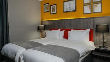 Et hotelværelse med en stor seng, et natbord, en lampe og et kunstværk på væggen.